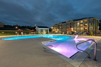 A lit up pool at night with a building in the background.